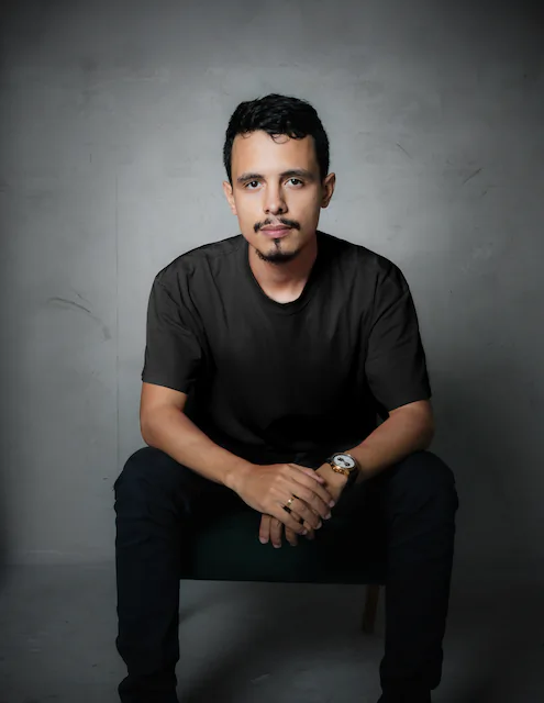 Gabriel da Silva Rodrigues, fotógrafo de eventos em Goiânia, sentado num estúdio de fundo cinza